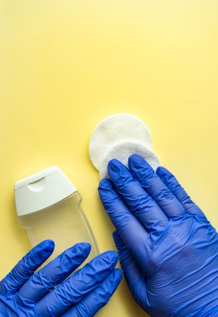 Top view of yellow table with hands wearing protective blue gloves holding soap and cotton with copy space