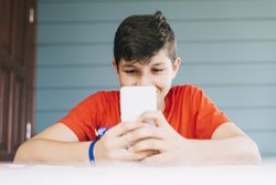 Teenage male wearing red t-shirt sitting outdoors using phone