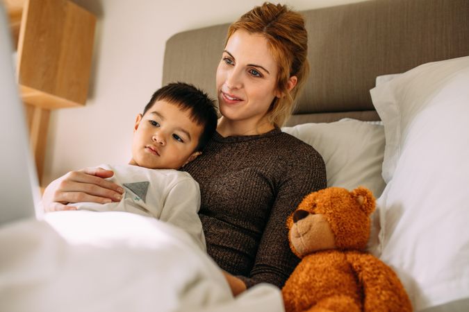 Beautiful mother with her cute son resting on the bed watching something interesting on laptop