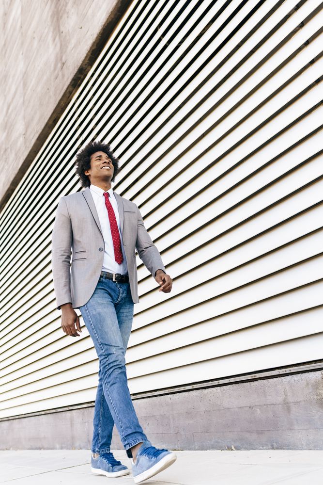 Man in jeans and dress shirt with tie walking next to wall