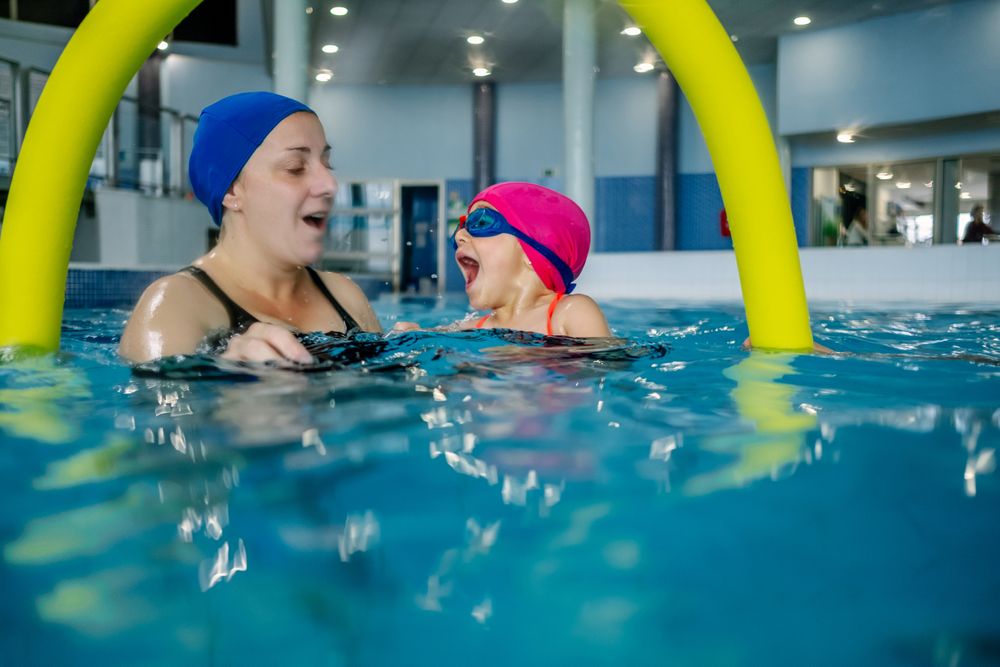 Cheerful girl swimming in pool with mother