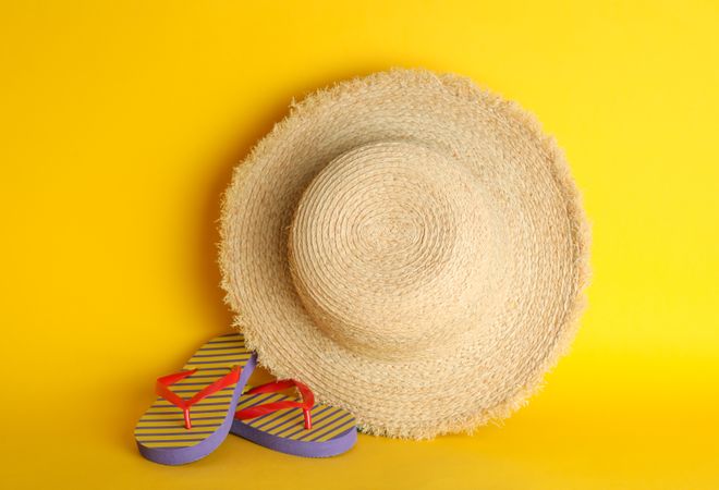 Straw hat and flip flops on color background, space for text. Summer accessories