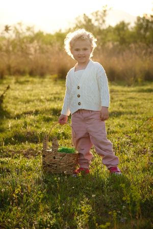 Smiling girl with basket standing on verdant grassy lawn