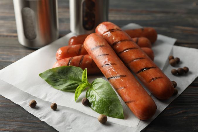Close up of grilled sausages or hot dogs with capers and basil