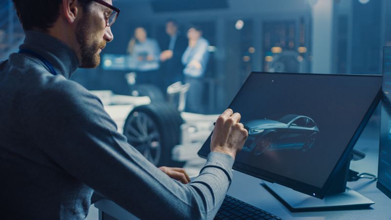 Professional Automotive Graphic Designer is Working on Concept Car Render with a Stylus Pen in a High Tech Innovative Laboratory with a Prototype Car Chassis.