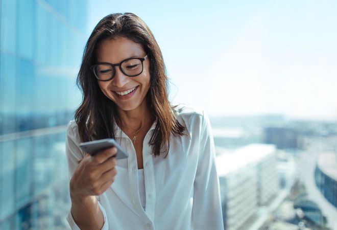 Woman wearing eyeglasses smiling while looking at her mobile phone
