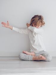 Boy in white pajamas leaning against the white wall of his house.