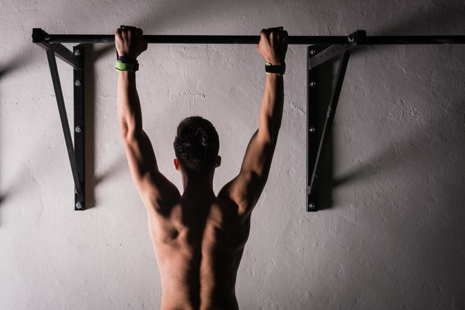 Man hanging on bar near wall in gym