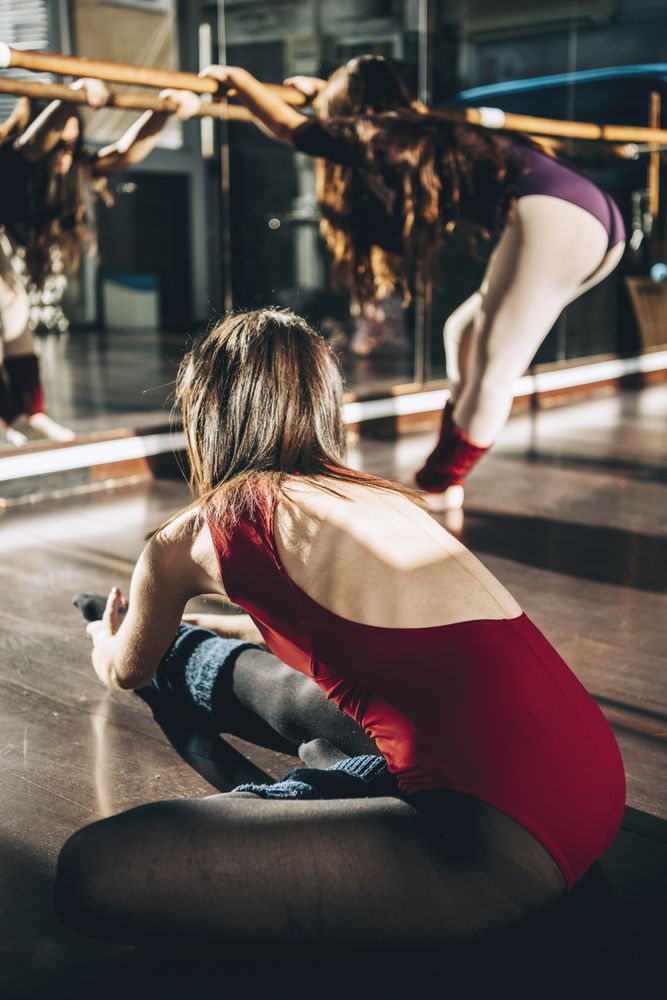 Young dancers training together in studio warming up and flexing in sunlight.