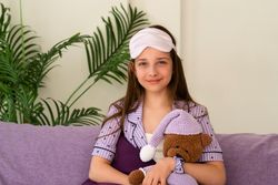 Girl with sleep mask pulled up, holding teddy bear