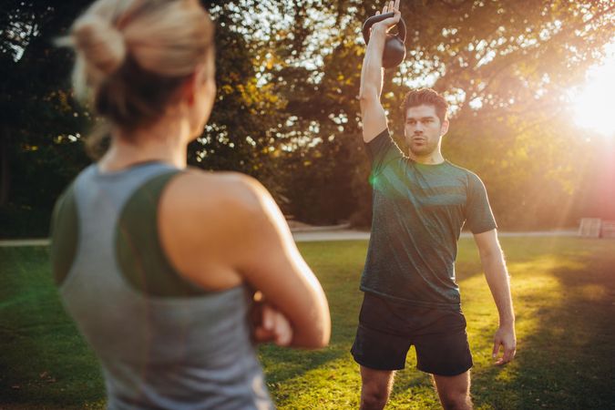 Healthy young man with female trainer exercising with kettlebell in the park