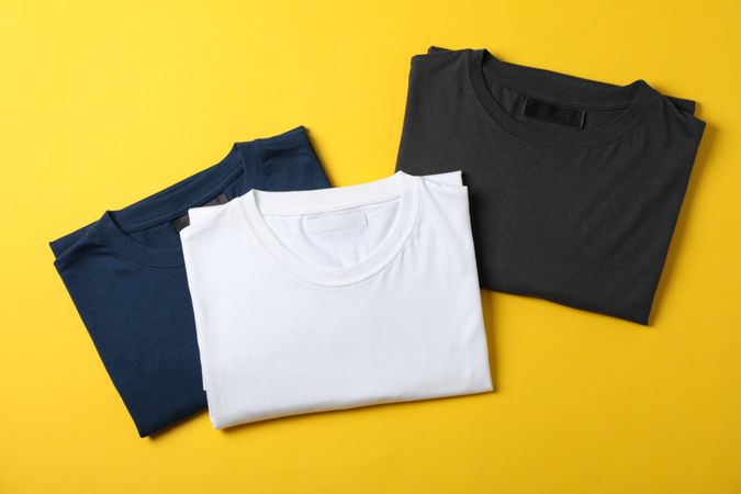 Folded blank t-shirts on yellow background, space for text