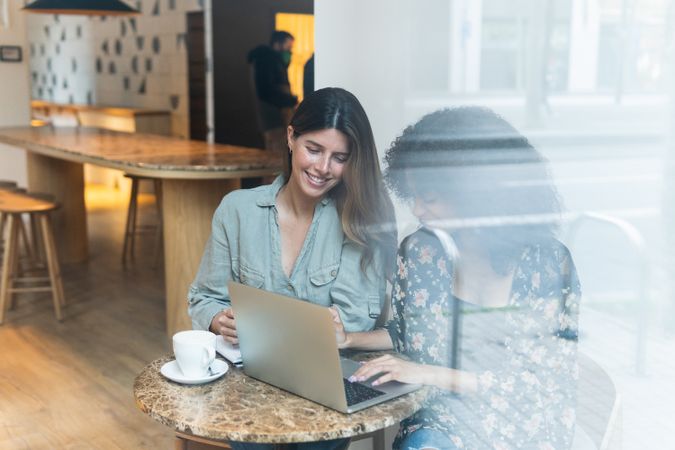 Smiling multiracial girlfriends sharing laptop in coffee shop