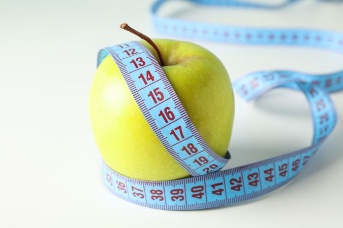 Apple with measuring tape on blank background, close up