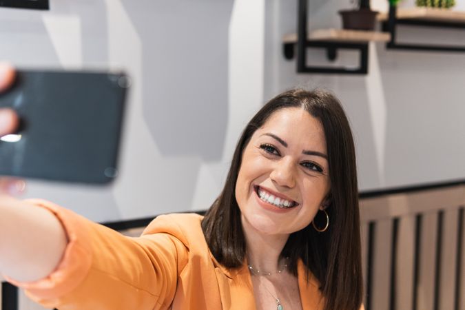 Cheerful woman taking selfie on smartphone in cafe