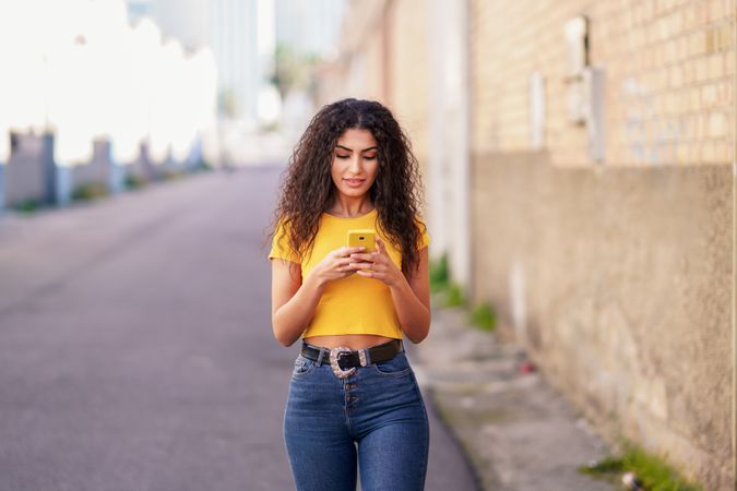 Female in yellow t-shirt walking on street with phone