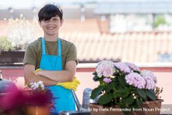 Young smiling teenager wearing gardening apron while standing with arms crossed on home terrace 5wXmO6