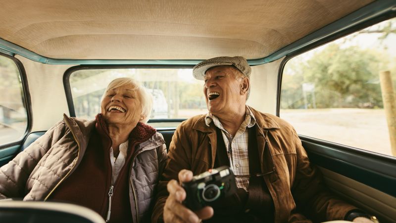 Cheerful mature couple sitting on backseat of their car and laughing