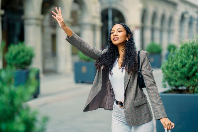 A Confident Young Woman Waving While Standing Outdoors in a Vibrant City Setting
