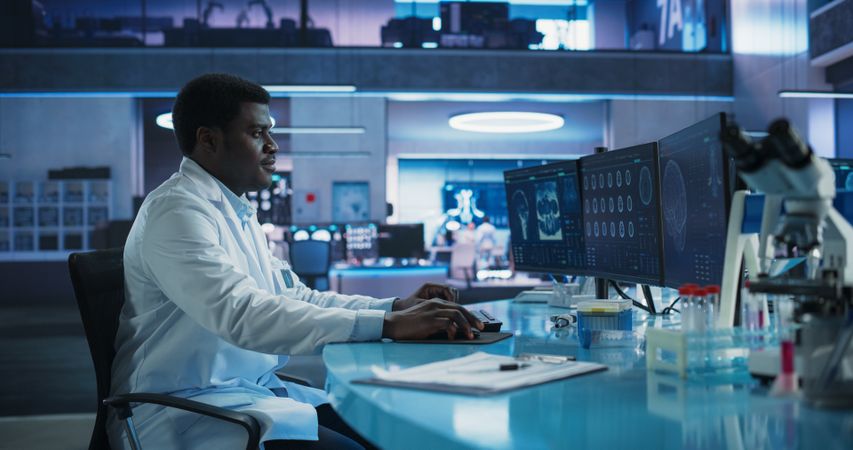 Black Male Neuroscientist Using Desktop Computer To Analyze MRI Scans Of Brain In Medical Research Center Laboratory.