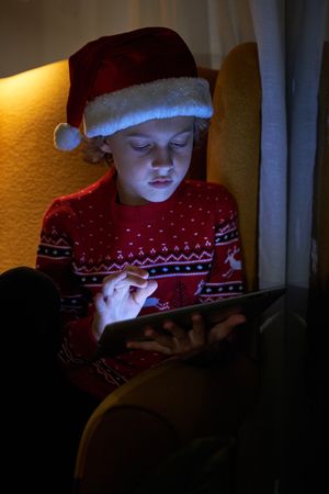 Little boy in Santa hat using tablet in dark room