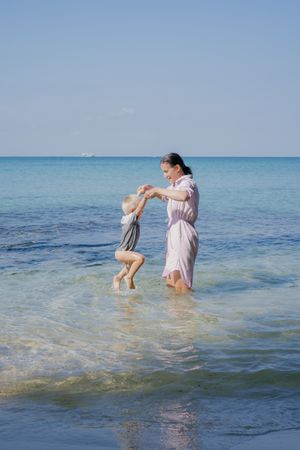 Woman and small kid having fun with water while relaxing on seacoast at resort