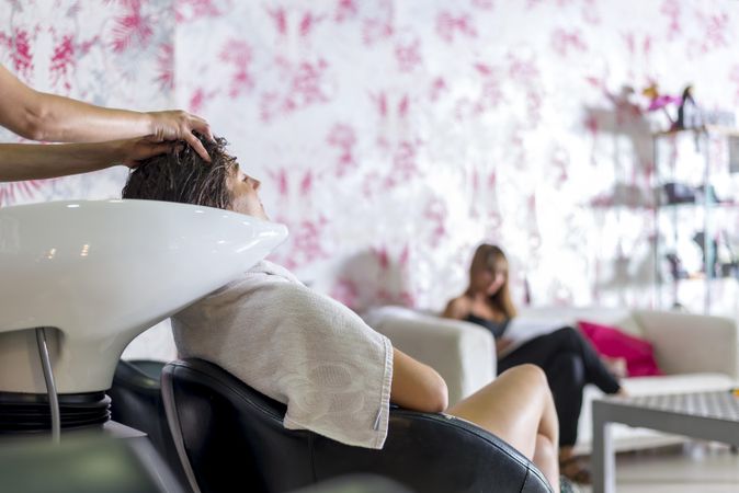 Woman having her hair washed in salon with another customer waiting