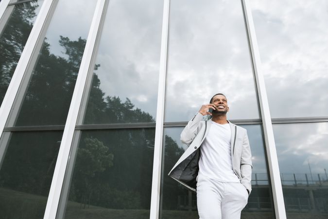 Elegant Black man talking smartphone leaning building