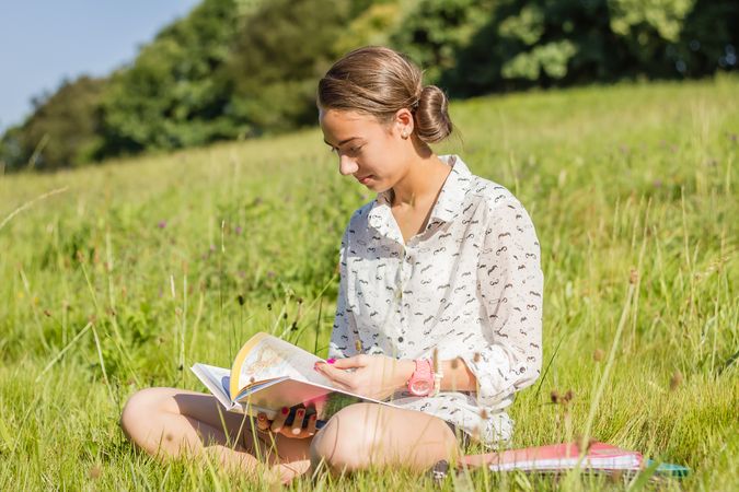young student reading a book in the park