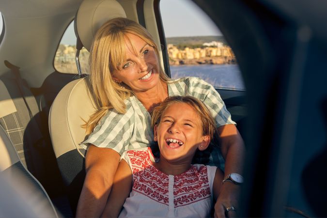 Blonde woman sitting inside a car with her daughter lying on top