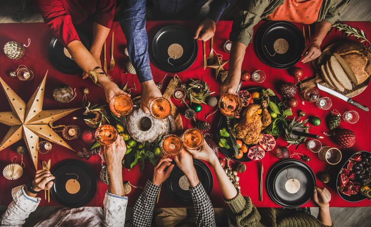 Group of people toasting with drinks at festive red table with cake, roast chicken, and decorations