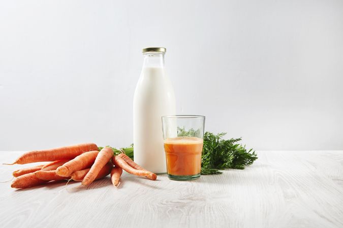 Bunch of carrots, bottle of milk and carrot juice on bright wooden table