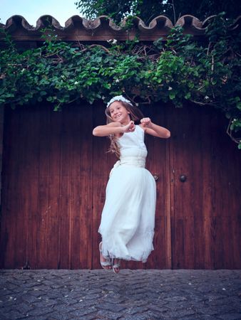 Cheerful young girl in white dress jumping near old entrance
