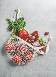 Top view of various vegetables and herbs in reusable plastic free shopping bag at grey concrete kitchen table