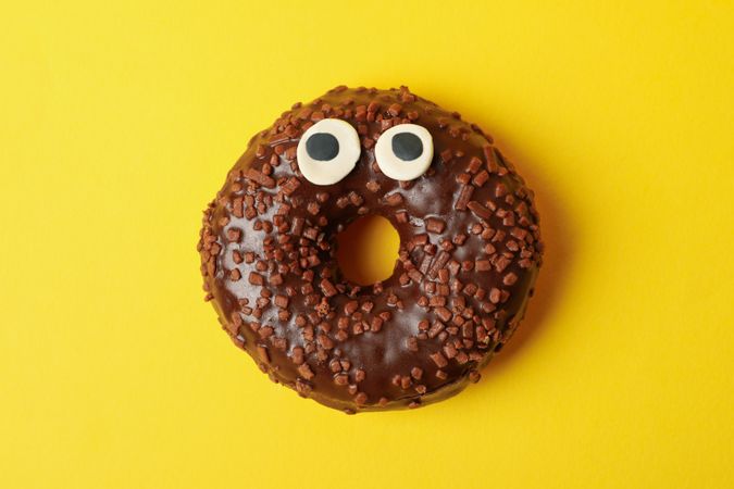 Tasty chocolate donut with eyes on yellow background