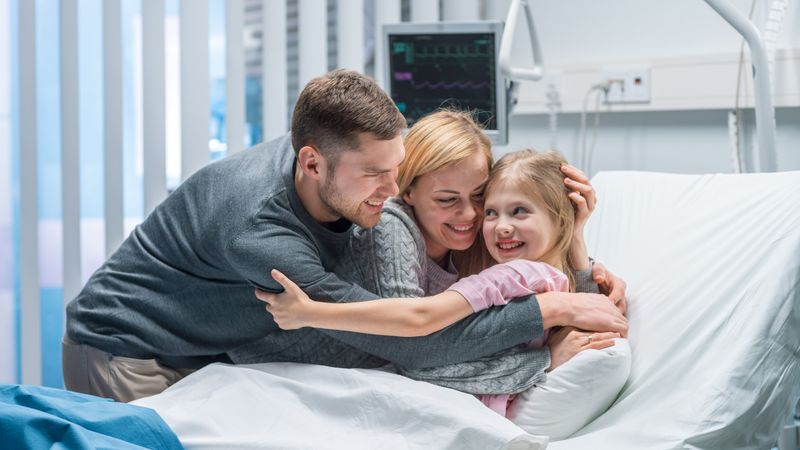 Portrait Shot of Happy Parents Hug Cute Little Girl Lying in the Hospital Bed