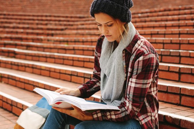 Young woman reading book on university stairs