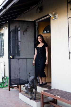 Full length portrait of woman in dark dress standing at her front porch with her dog