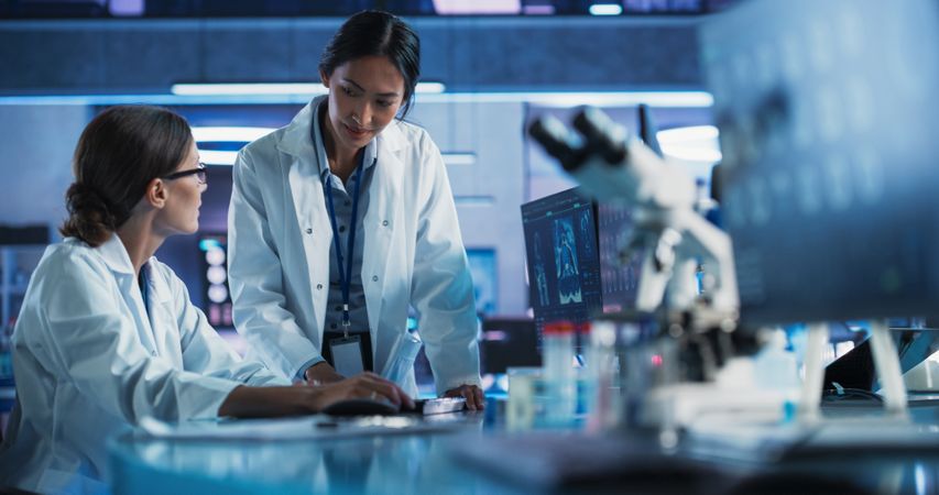 Medical Hospital Research Laboratory: White And Asian Female Scientists Talking And Using Desktop Computer With CT Scans Of Human Brain.
