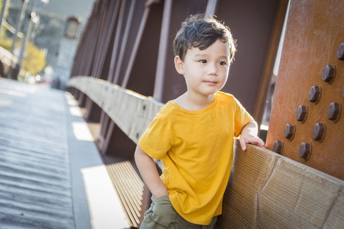 Biracial Boy Leaning on Bridge Outdoors