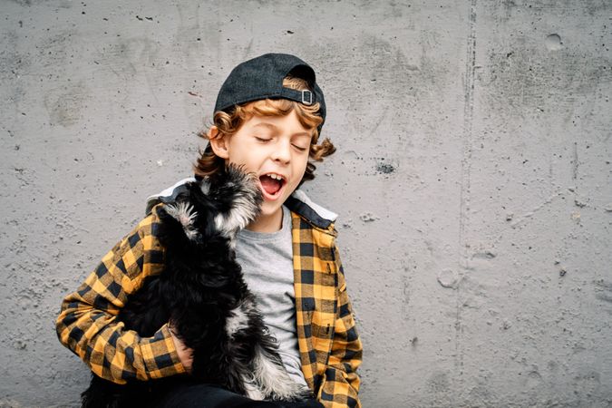 Kid holding dog and yawning against concrete wall