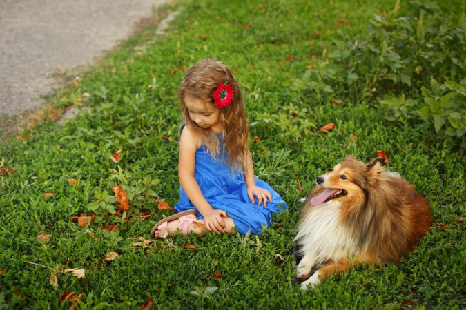 Female child in blue dress sitting with dog in the grass