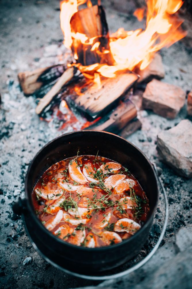 Pot of soup sitting next to an open camp fire