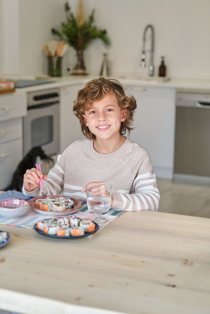 Smiling boy having delicious sushi for lunch at home