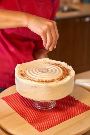 Crop female sprinkling cake with cinnamon powder
