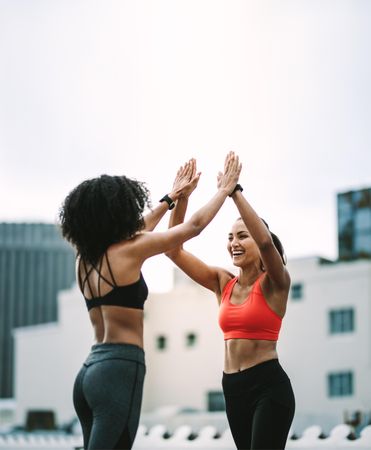 Side view of two fitness women giving high five standing on rooftop