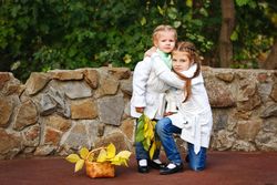 Big sister hugging her little sister in front of stone wall in park
