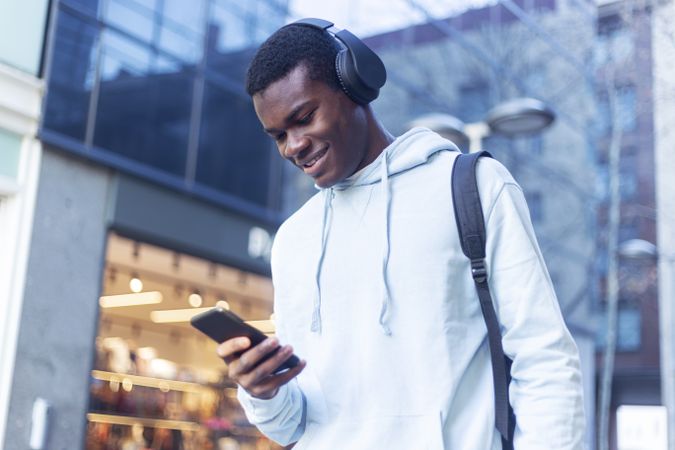 Young Black man standing in the street while listening music on headphones