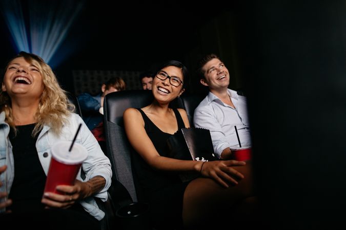 Smiling young woman watching movie with friends in cinema hall