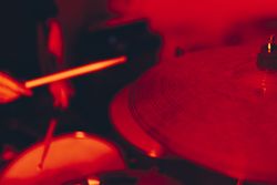 Anonymous man with drumsticks playing on drums in redness